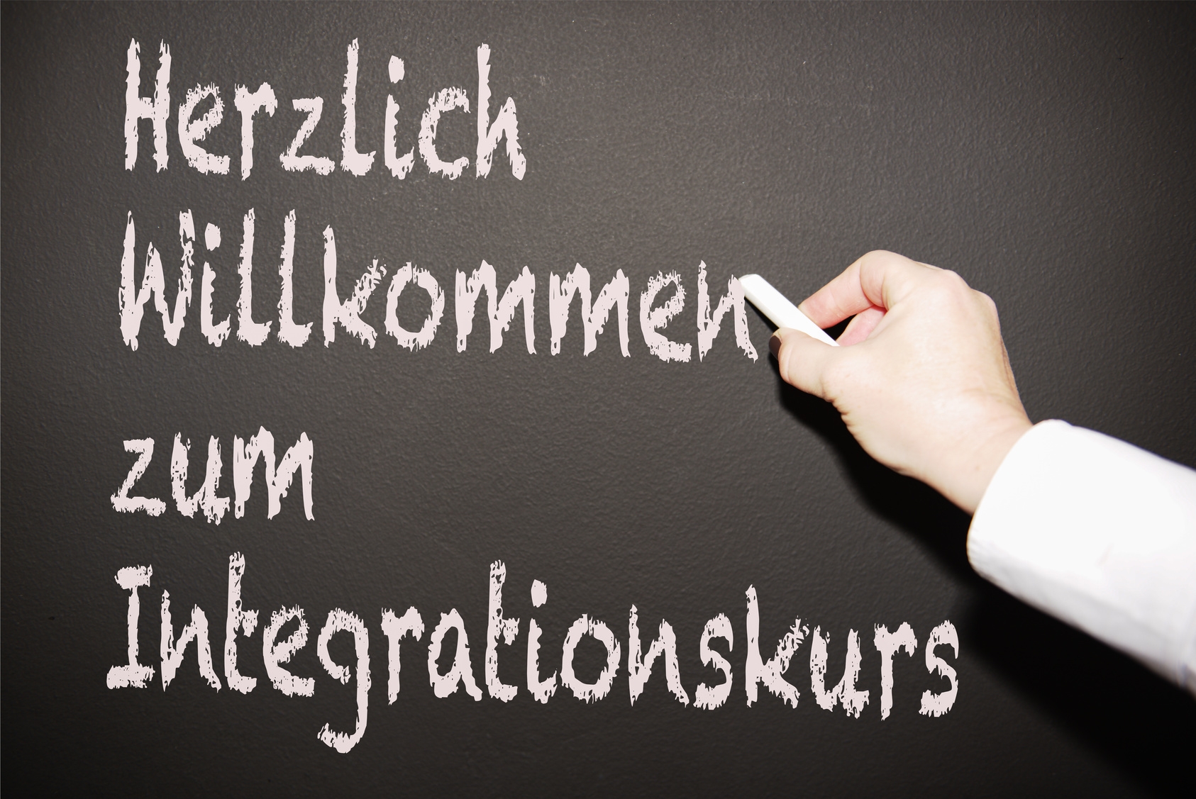 Lehrerin scheibt an die Tafel "Herzlich willkommen zum Integrationskurs"