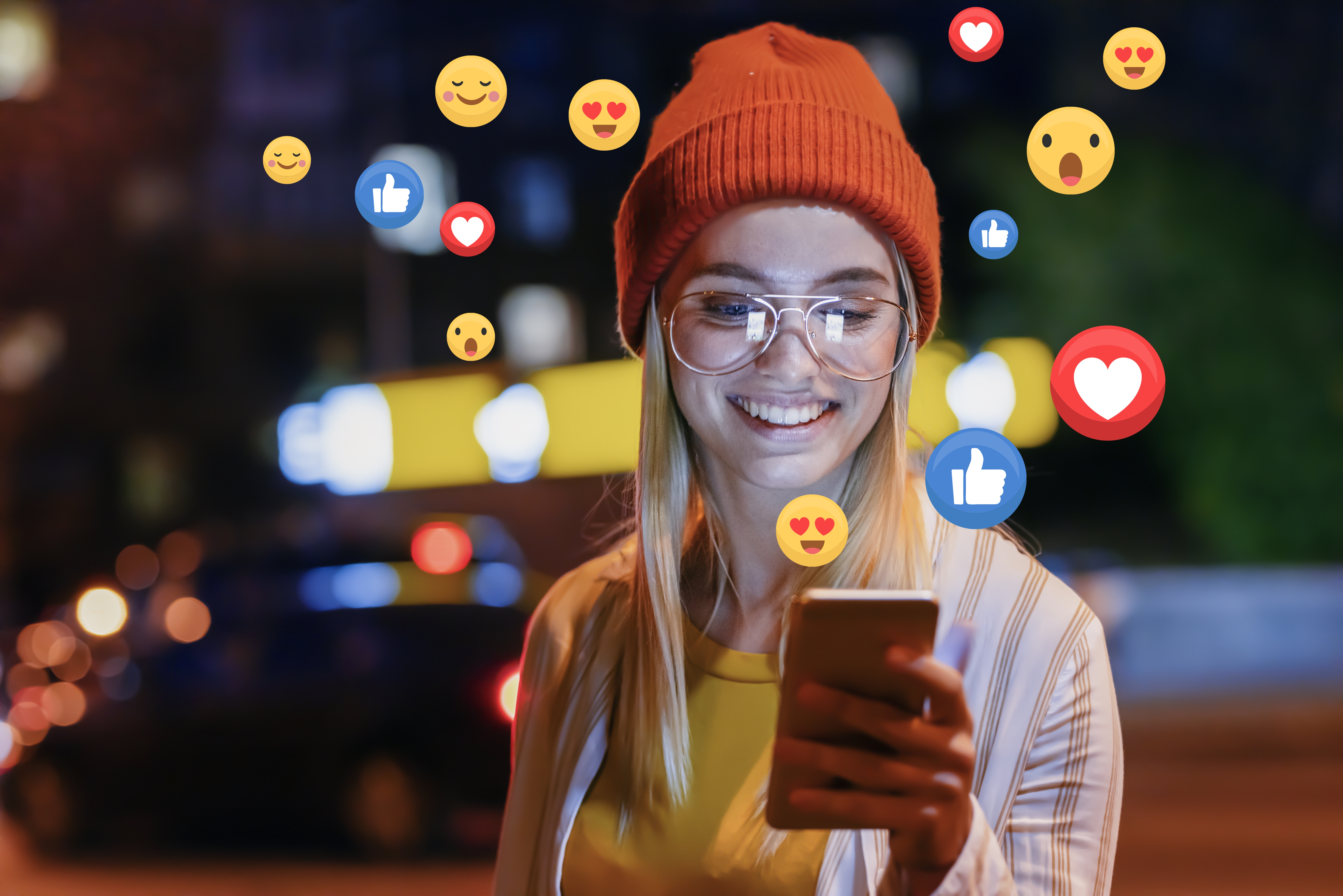 Junge Frau hält ein Smartphone in der Hand. Aus dem Smartphone strömen Emojis und Emoticons.