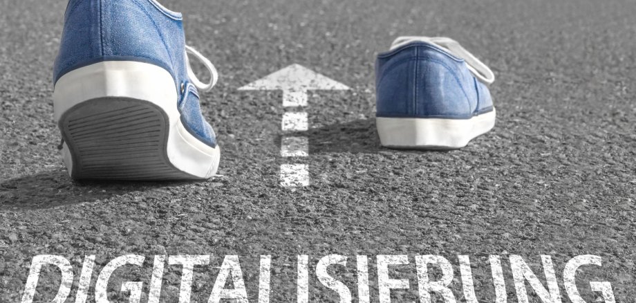 Auf Straße steht das Wort "Digitalisierung". Darüber ist ein weißer Pfeil gezeichnet. Zwei Schuhe gehen in die Richtung des Pfeils.