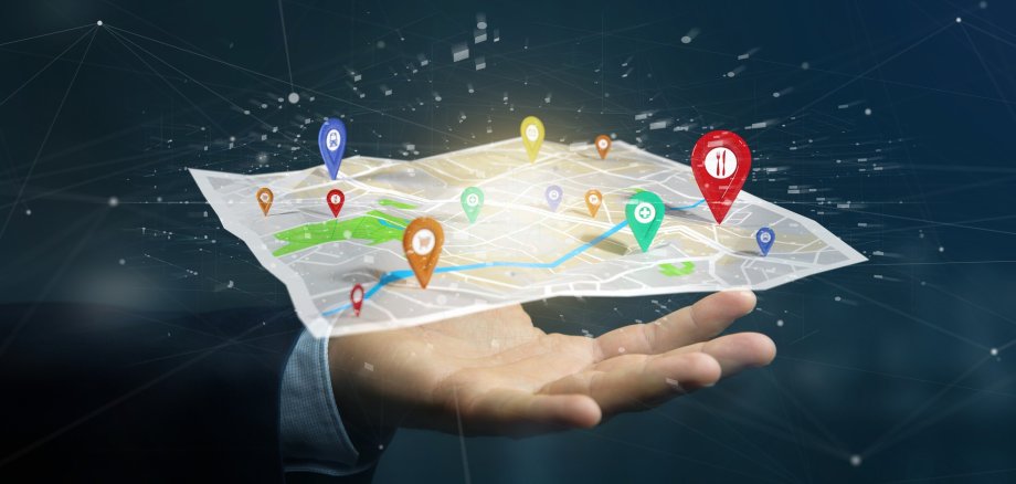 Auf der Hand eines Geschäftsmann liegt eine 3D-Stadtkarte mit markierten Orten. Das Konzept einer Smart City soll so dargestellt werden.