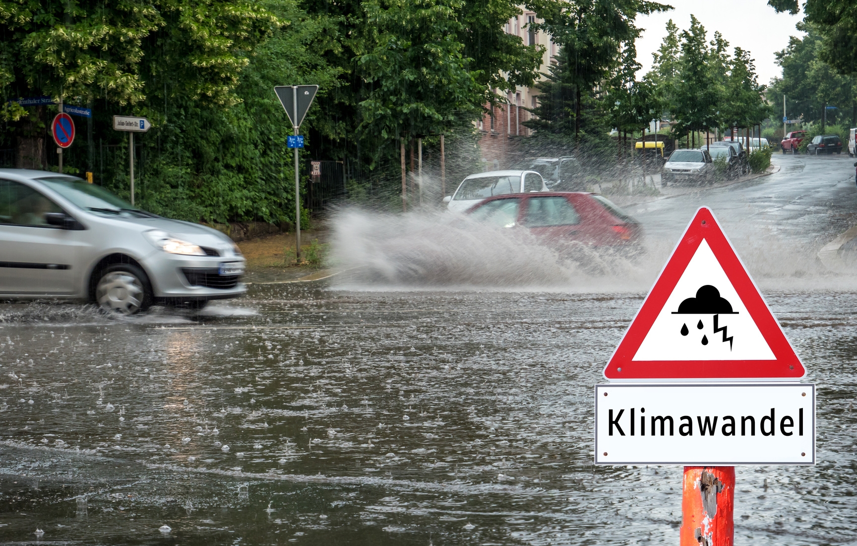 Ein Auto fährt durch eine überflutete Straße und vorne steht das Schild mit der Aufschrift "Klimawandel". Ein Auto fährt durch eine überflutete Straße und vorne steht das Schild mit der Aufschrift "Klimawandel".