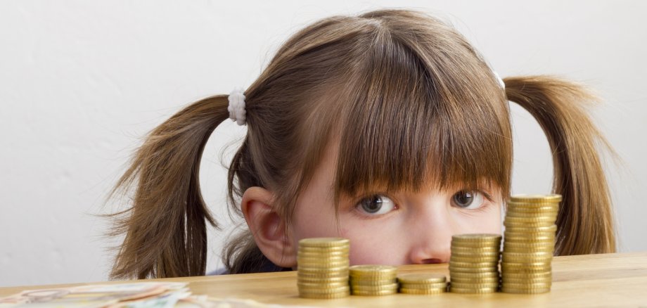 Mädchen schaut auf Geldtürme - auf dem Tisch liegend