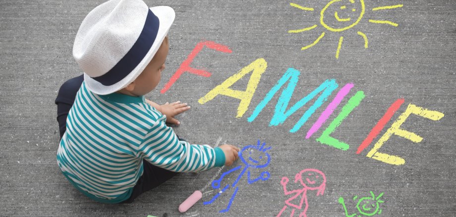 Ein Kind, das mit Straßenkreide "Familie" auf die Straße schreibt.