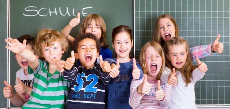  Freude von Kindern vor einer Tafel, auf der "Schule" steht.