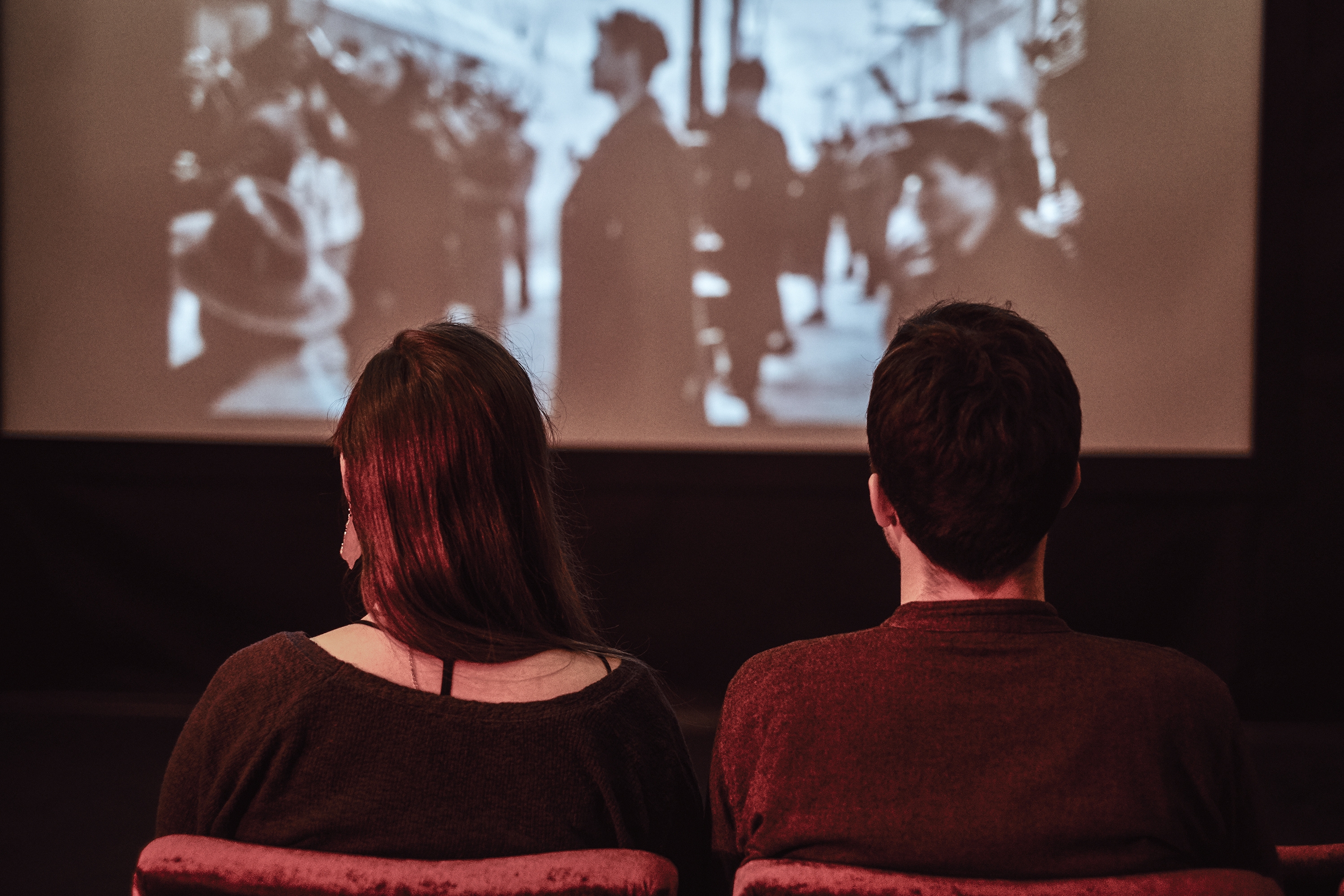 Zwei Personen, die einen Schwarz-Weiß-Film auf Leinwand/im Kino ansehen. Zwei Personen, die einen Schwarz-Weiß-Film auf Leinwand/im Kino ansehen.