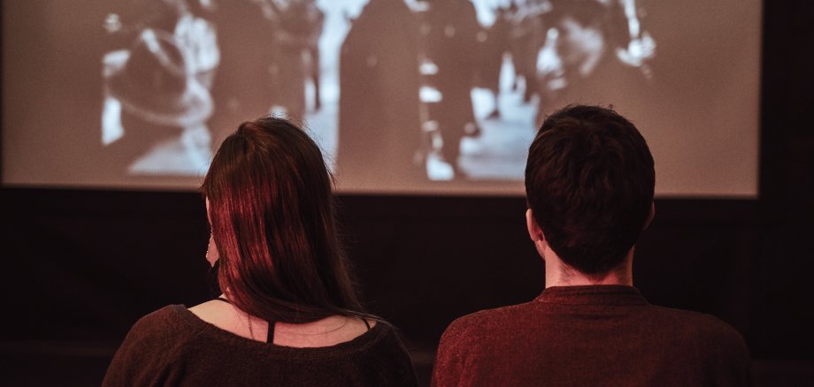 Zwei Personen, die einen Schwarz-Weiß-Film auf Leinwand/im Kino ansehen.