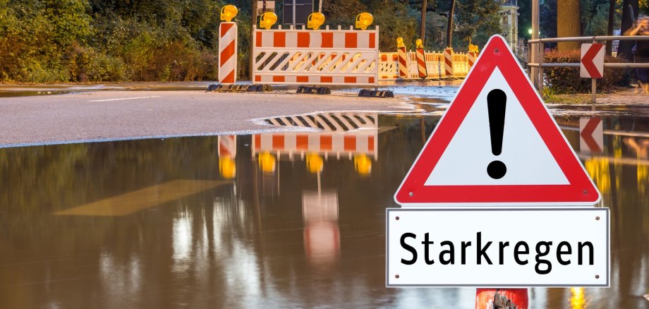 Überschwemmte Straße mit Warnschild Starkregen