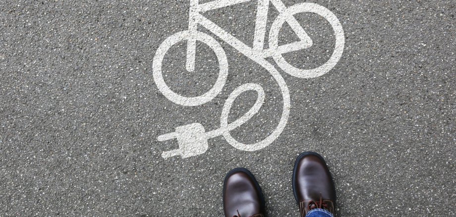 E-Bike Symbol auf der Straße, Person steht davor