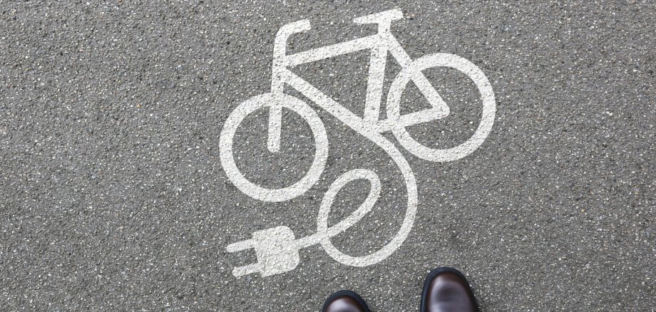 E-Bike Symbol auf der Straße, Person steht davor