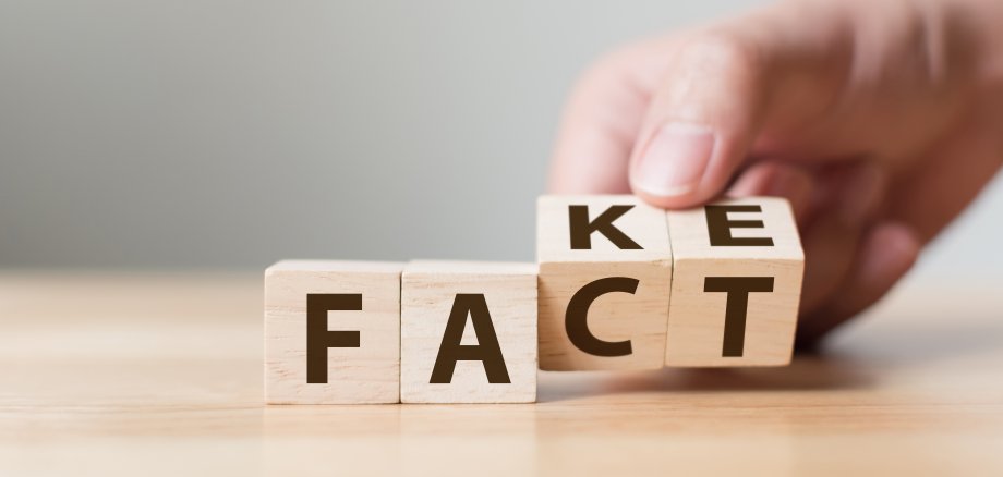 Auf Würfeln stehen die Worte "Fact" und "Fake". Eine Hand dreht die letzten beiden Würfel und verändert so das Wort.