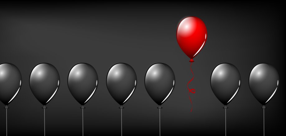 Eine Reihe schwarzer, schwebender Luftballons wird unterbrochen von einem roten Luftballon, der etwas höher schwebt