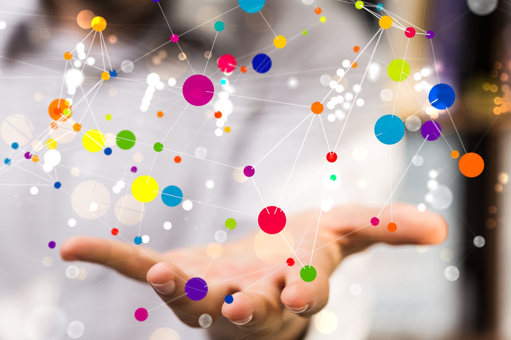 Eine nach vorne ausgestreckte Hand über der eine Vielzahl verschieden großer Punkte abgebildet sind, welche durch weiße Linien verbunden sind.