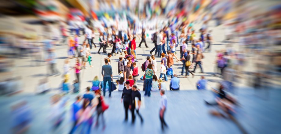 Viele Menschen in einer Fußgänger-Zone. Das Bild wird von der Mitte ausgehend immer unschärfer.