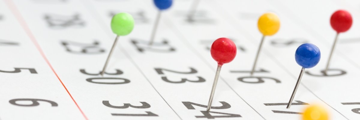 Kalender mit zahlreichen bunten Stecknadeln, welche zur Markierung auf einzelnen Daten pinnen.