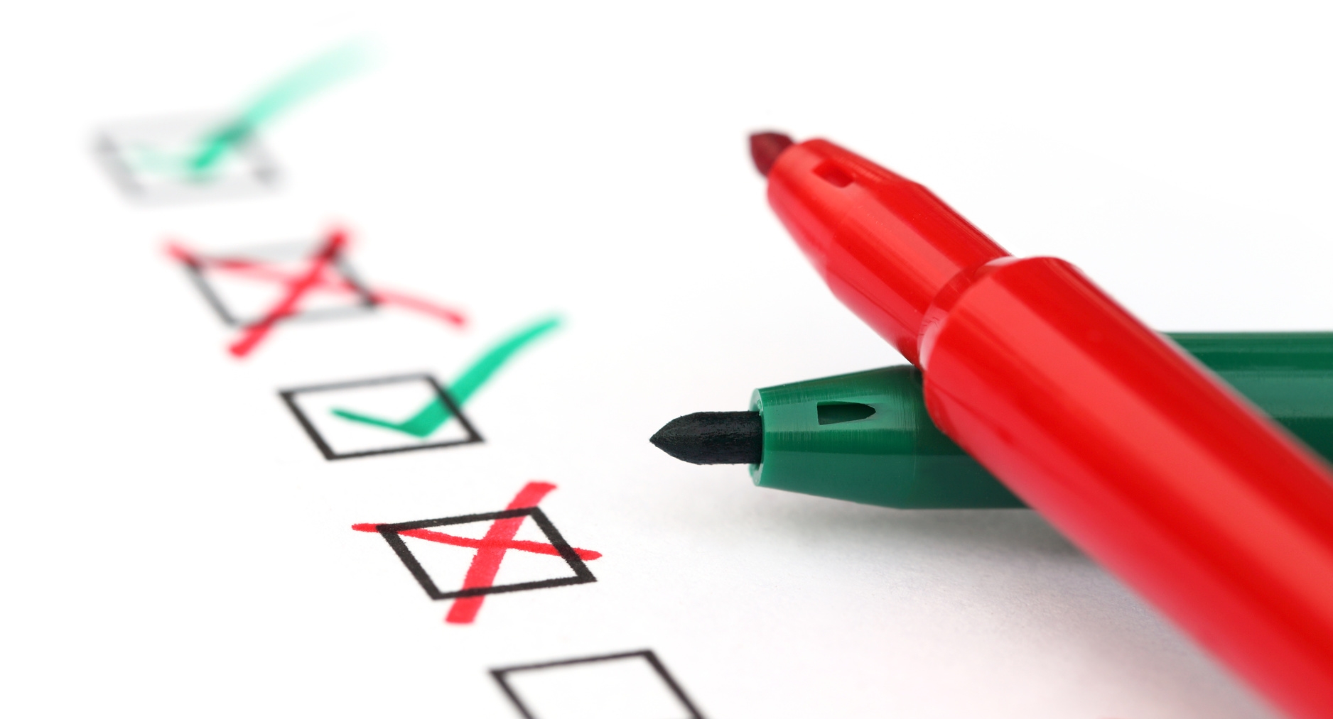 Auf einem Blatt sind untereinander Kästchen abgedruckte , welche entweder rot oder grün angekreuzt wurden. Ein offener, roter und ein offener, grüner Stift liegen auf dem Blatt.