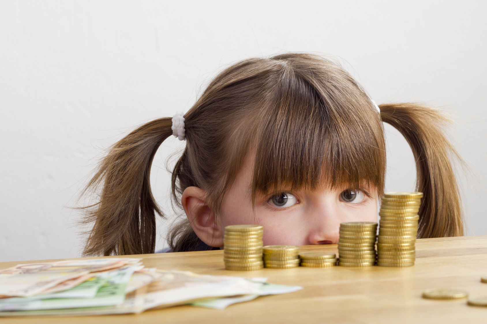 Mädchen schaut auf Geldtürme - auf dem Tisch liegend Mädchen schaut auf Geldtürme - auf dem Tisch liegend