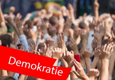 Menschen auf einem Konzert mit gehobenen Händen. Im Vordergrund ein roter Balken mit der Aufschrift "Demokratie". Menschen auf einem Konzert mit gehobenen Händen. Im Vordergrund ein roter Balken mit der Aufschrift "Demokratie".