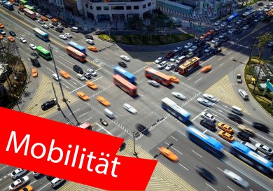 Vogelperspektive auf eine Straßenkreuzung. Im Vordergrund ein roter Balken mit der Aufschrift "Mobilität". Vogelperspektive auf eine Straßenkreuzung. Im Vordergrund ein roter Balken mit der Aufschrift "Mobilität".